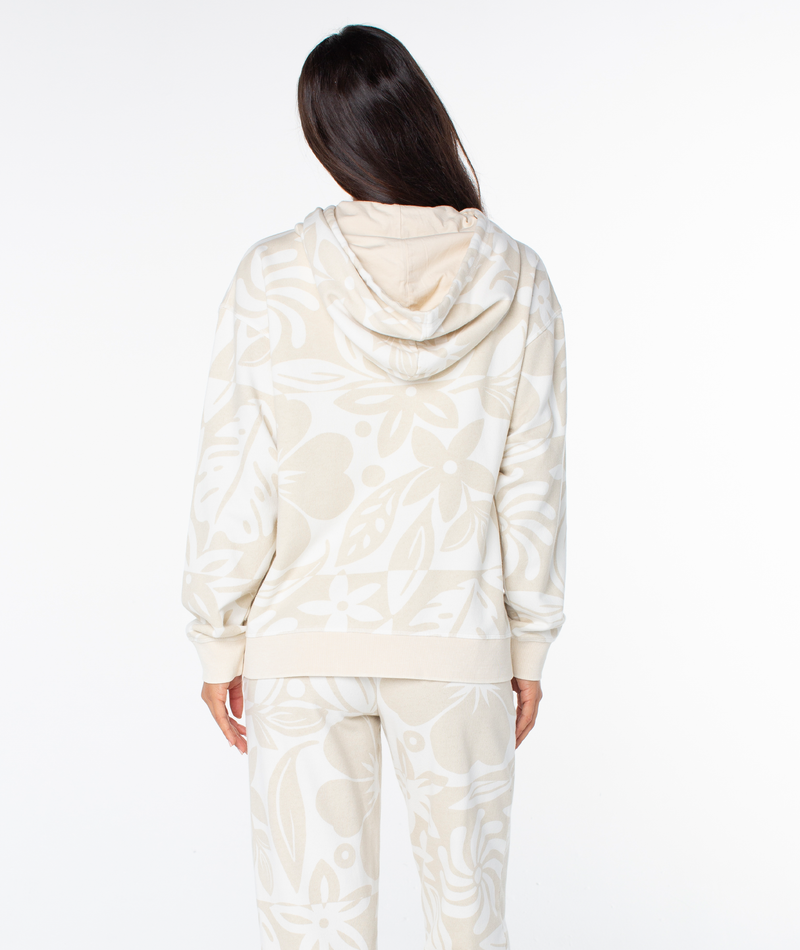 View from behind of a person in a Roxy Maile Printed Hoodie and matching pants, both in an oversized cream color with a large white tropical floral print.