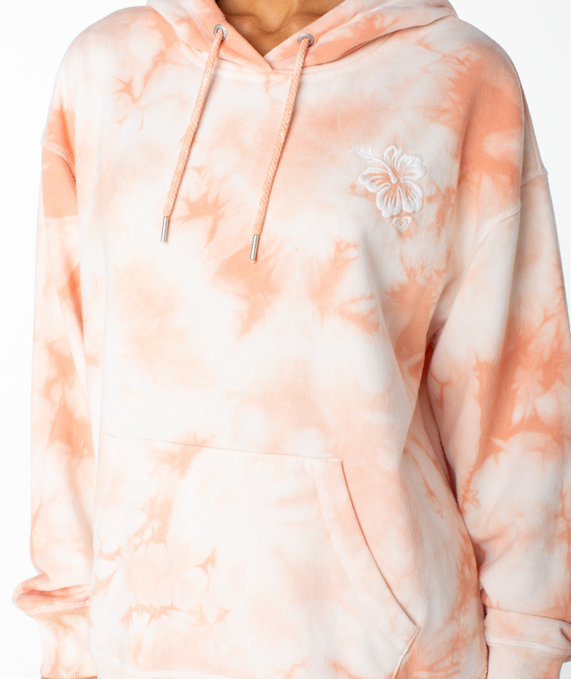 A person is wearing the Roxy Maile Tie Dye Hoodie, featuring a peach and white tie-dye pattern, front pocket, and an embroidered hibiscus flower on the chest. This cozy cotton sweatshirt is perfect for loungewear. The lower face is not visible.