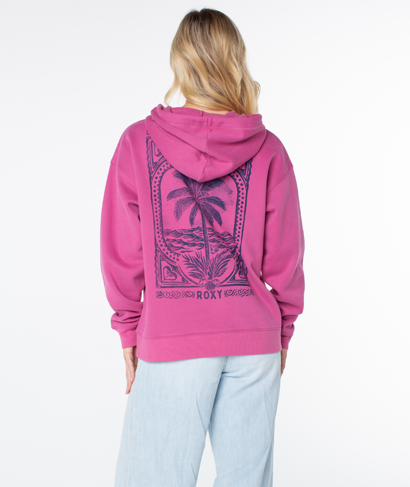 A blonde woman wears the Roxy Raya Hoodie, an oversized pink sweatshirt with navy palm tree graphics on the back, styled with light blue jeans against a plain white background.
