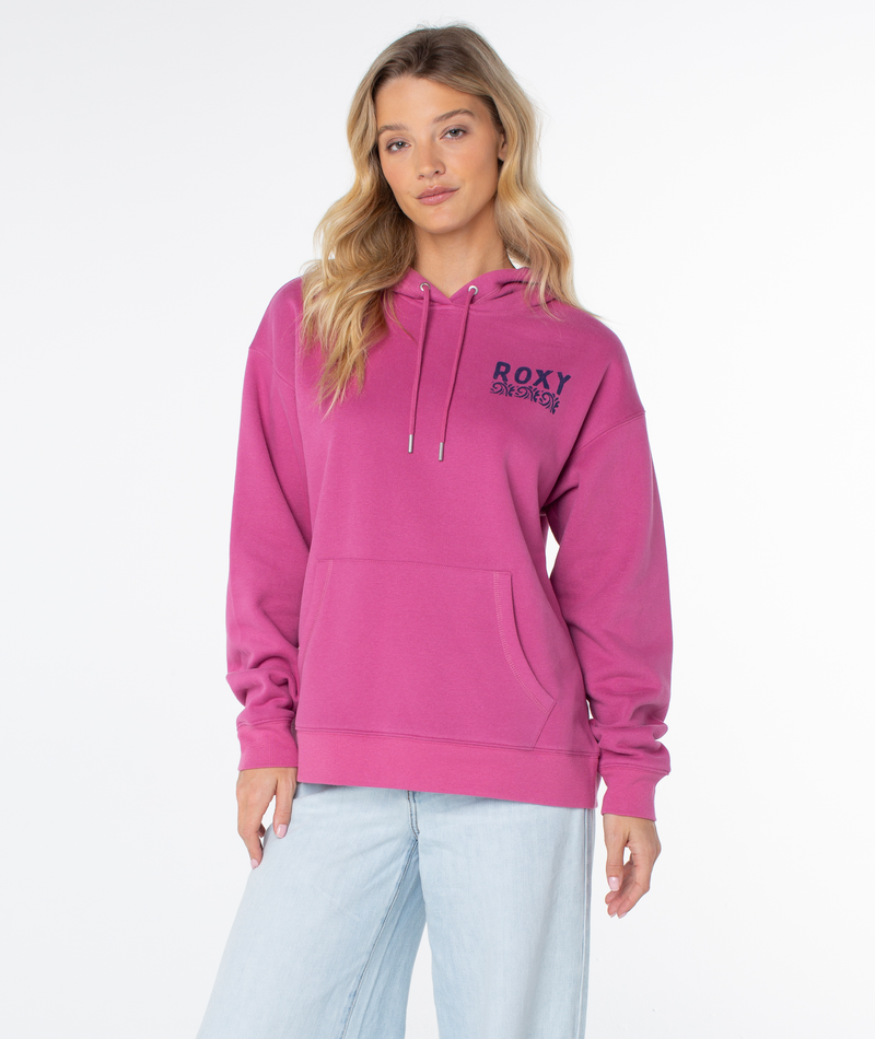 A woman wears an oversized magenta Raya Hoodie by Roxy with chest graphics and ROXY text, paired with light blue jeans, standing against a plain white background.