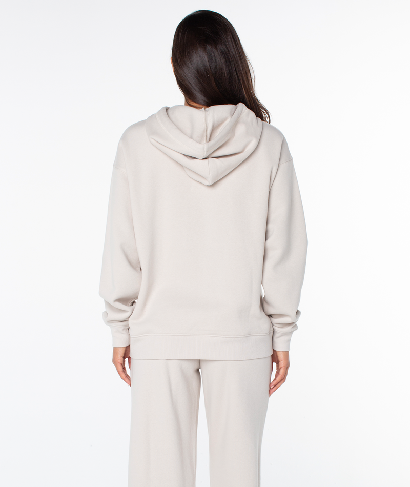 A person with long brown hair wears an oversized Raya Hoodie by Roxy and matching pants, facing away from the camera against a white background.