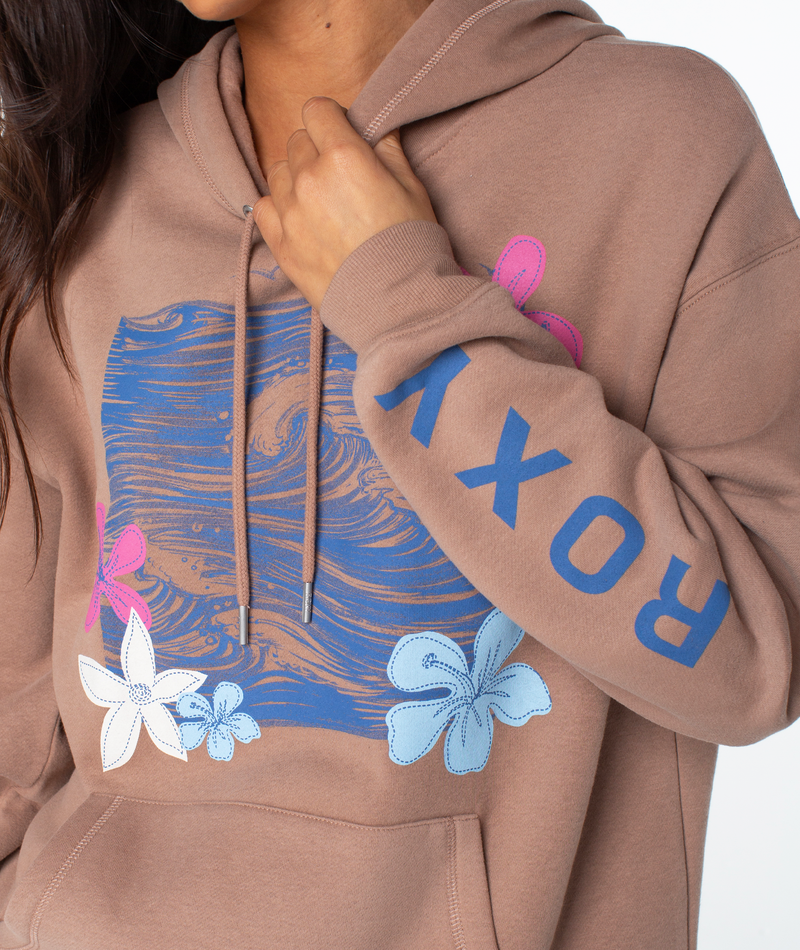 A person holds the Raya Hoodie by Roxy, featuring a brown color, blue and pink floral wave graphic on the front, and ROXY in blue lettering down the sleeve.