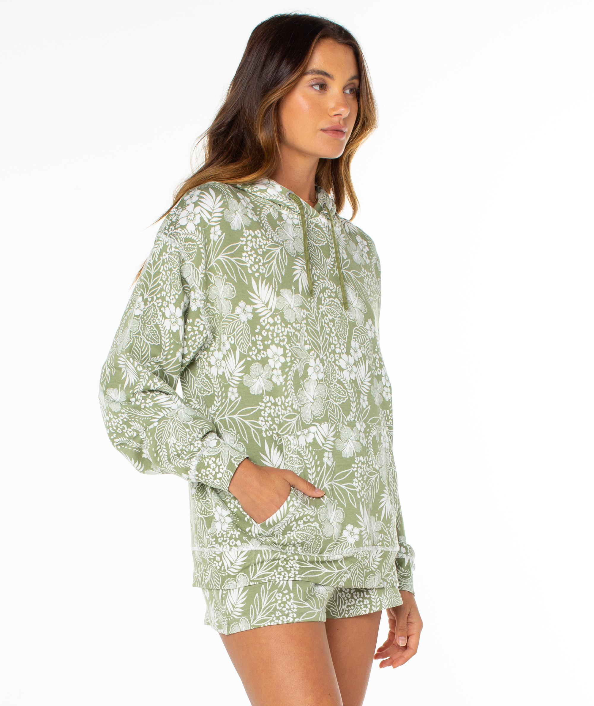 A woman poses against a plain white background, wearing the Roxy Surfing By Moonlight Printed Hoodie in light green with a white floral pattern, made from soft modal stretch fabric for comfort and style.