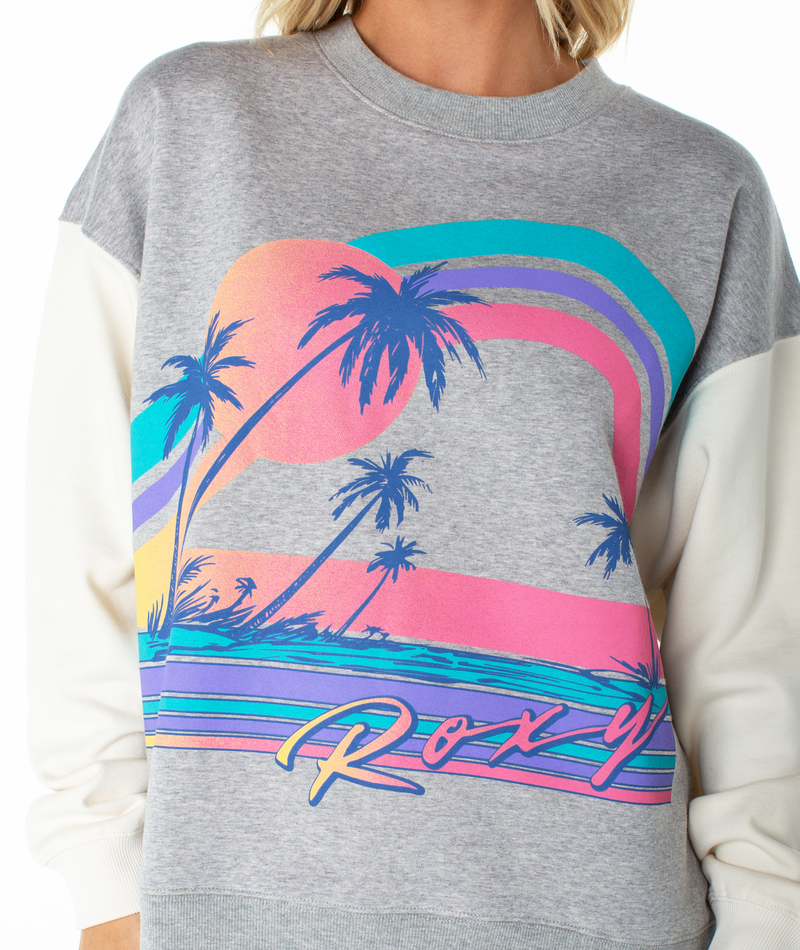 Wearing the Roxy Lineup Contrast Crew, an oversized gray crewneck sweatshirt with white sleeves and a retro color block design featuring palm trees, a sunset, curved stripes, and "Roxy" across the front.