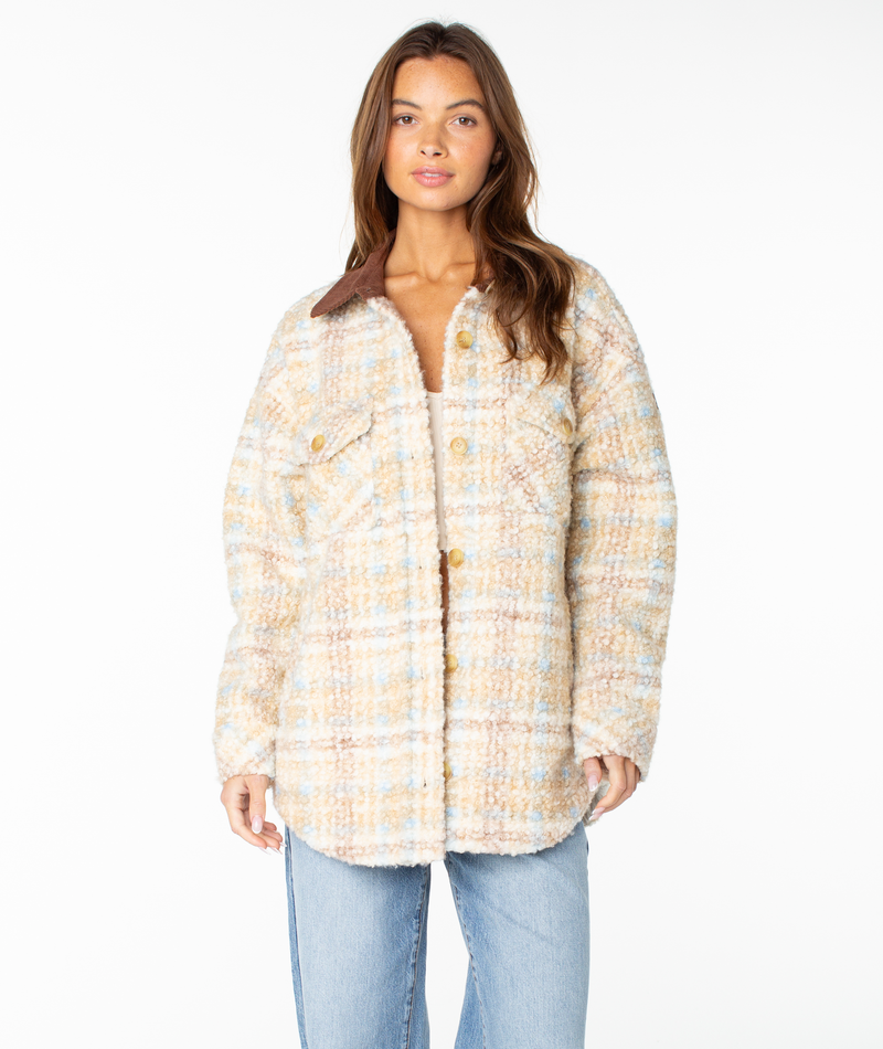 A woman models the Roxy Overlander Jacket, featuring a textured pastel plaid design with large buttons and a brown collar, styled with light blue jeans against a plain white background—a flannel-inspired fall essential.