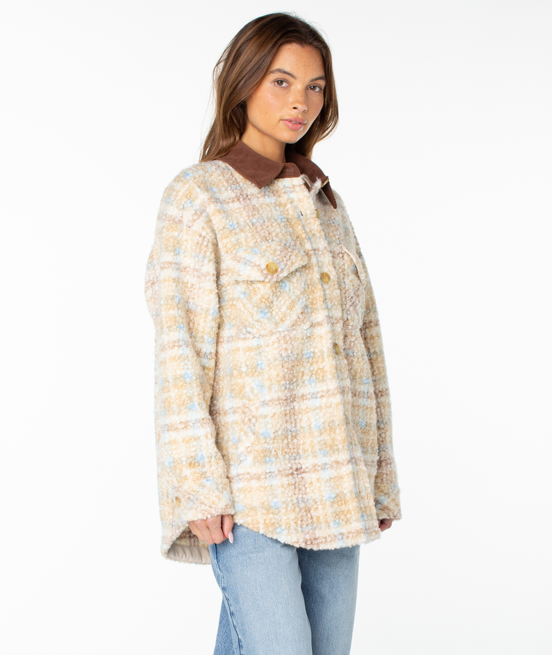 A woman wears the Roxy Overlander Jacket in Pebble Tartan Plaid, featuring a brown collar and gold buttons, paired with light blue jeans and standing against a white background. This flannel-inspired piece is the perfect fall staple for any wardrobe.