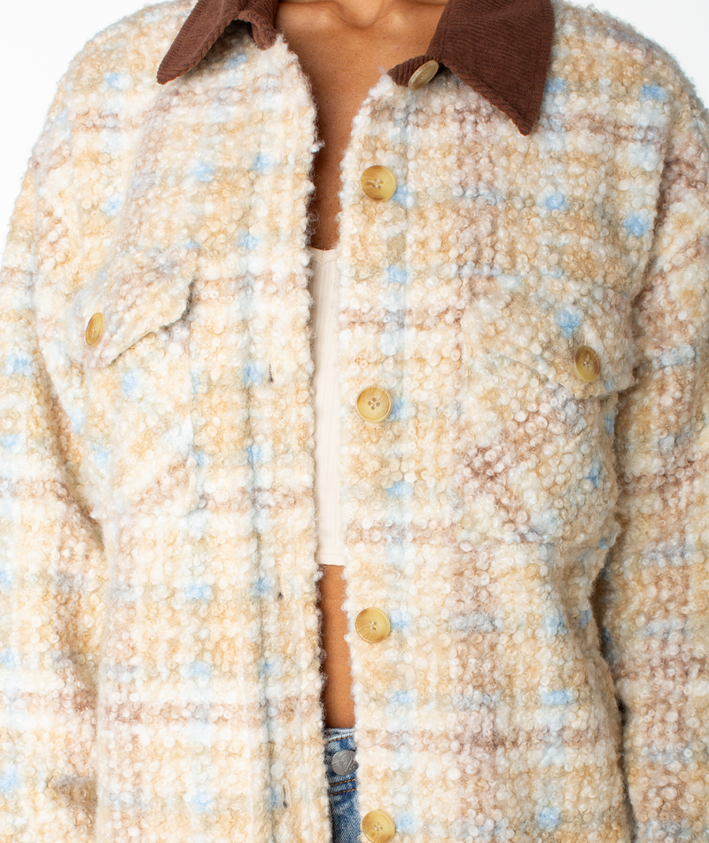 A person wearing the Roxy Overlander Jacket, featuring a textured, flannel-inspired plaid design with large buttons and a brown collar, layered over a beige top. Only the torso and part of the face are visible—this piece is a true fall staple.