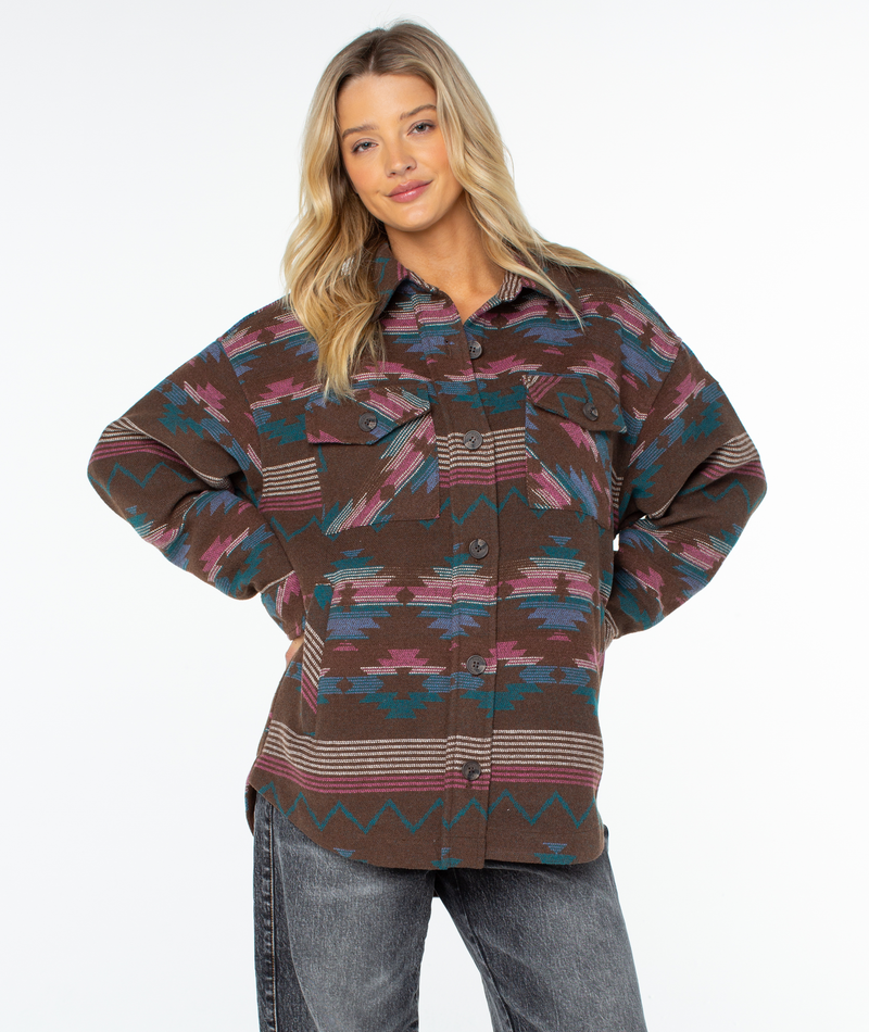 A woman wearing an oversized, brown Roxy Overlander Jacket with a geometric, multicolored pattern and two chest pockets.