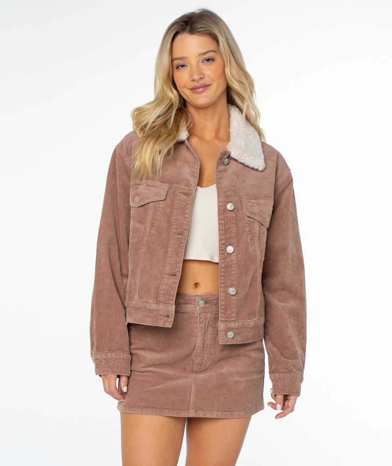 Woman wearing a Roxy Big Smoke Jacket in Ginger Snap Solid with a white sherpa collar and matching skirt, standing against a plain white background.