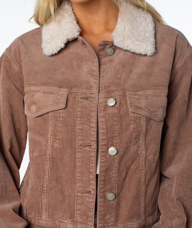Someone wears the Roxy Big Smoke Jacket, a light brown corduroy blend with a sherpa collar, silver buttons, and two chest pockets. The jacket is partially buttoned up.
