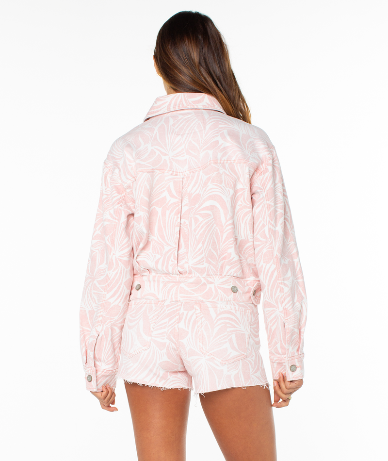 A woman with long brown hair faces away, wearing the Roxy Up To Putty Jacket in light pink and white print with matching frayed shorts, set against a plain white background.