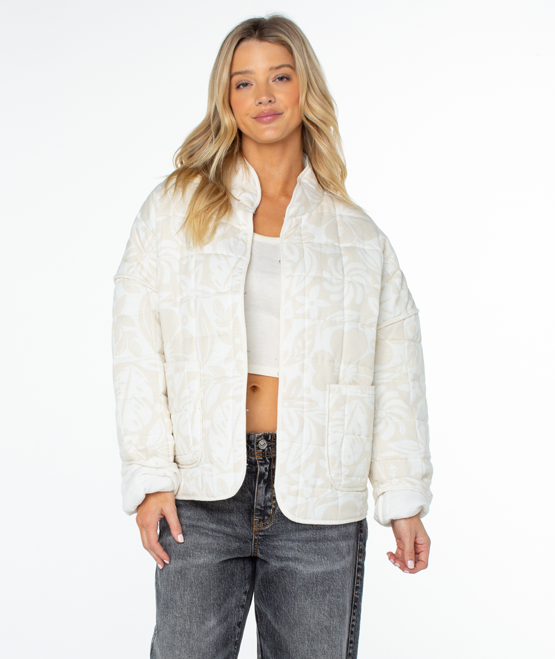 A person wearing a relaxed-fit, cream-colored, quilted Roxy Solana Jacket with a floral pattern, a high collar, and two front patch pockets.