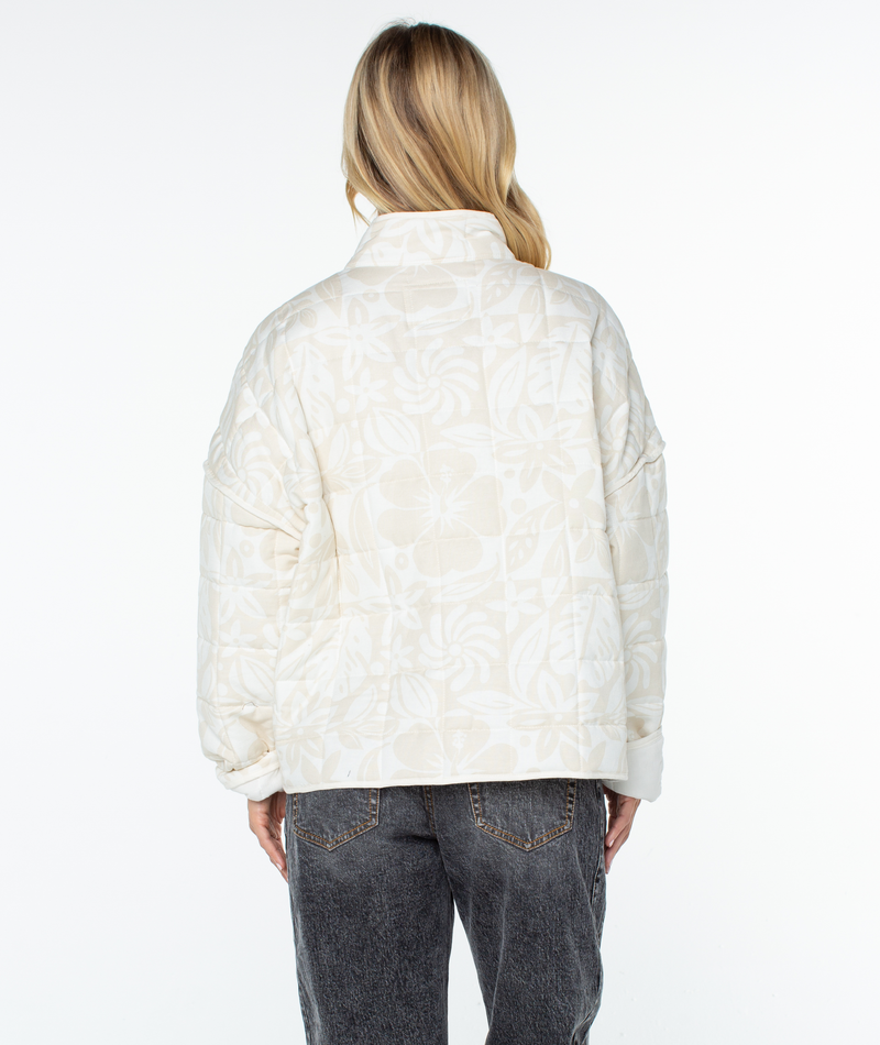 Back view of a person wearing a relaxed fit, cream-colored Roxy Solana Jacket with a subtle floral print and dark gray jeans.