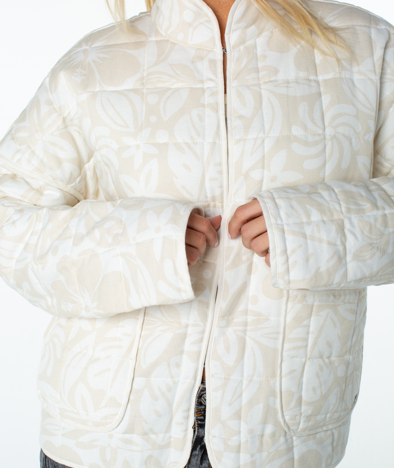 A person wearing a relaxed fit Roxy Solana Jacket, a zip-up, cream-colored quilted piece featuring a light beige leaf pattern.