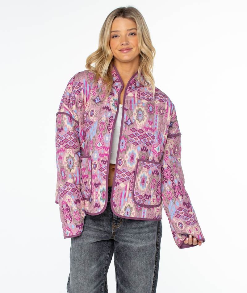 A person wearing a relaxed fit Roxy Solana Jacket with a purple, pink, and blue geometric pattern and two front pockets.