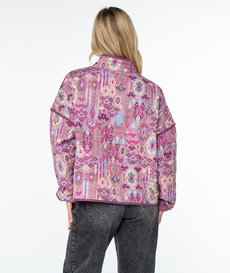 Back view of a person wearing a relaxed fit Roxy Solana Jacket, a quilted, high-neck piece featuring a colorful, patterned geometric print in shades of pink and purple.