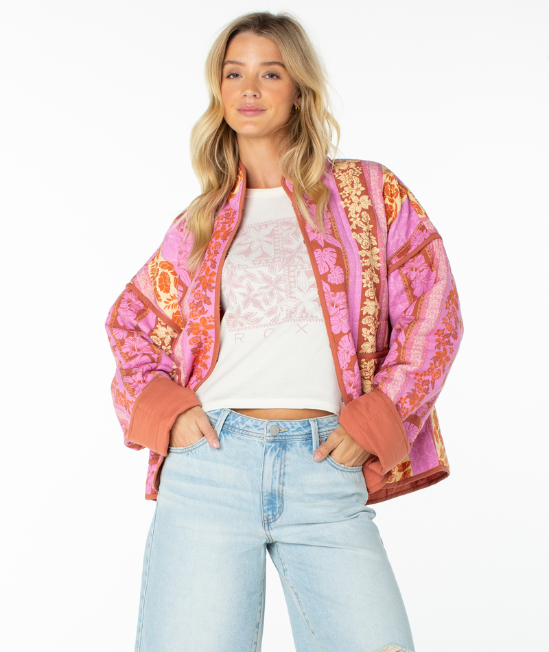 A woman with long blonde hair wears the Roxy Solana Quilted Jacket over a white graphic t-shirt and light blue jeans, standing with hands in pockets against a plain white background—a perfect fall staple.