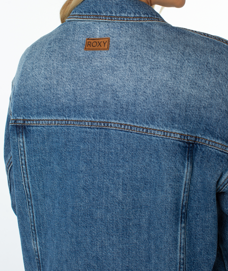 Back view of a blue denim Roxy Lost Treasure Jacket with a brown brand patch at the center of the collar.