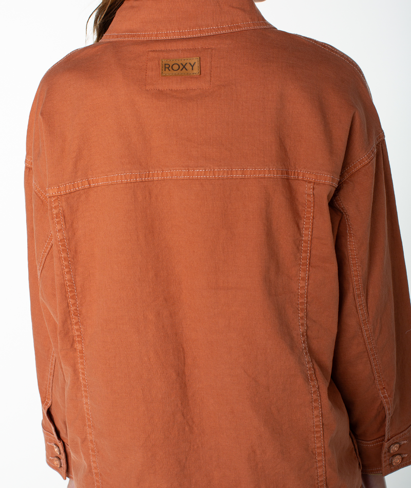 A person wearing the Roxy Lost Treasure Jacket, a rust-colored, vintage-inspired piece featuring a visible Roxy label on the upper back, photographed from behind against a plain white background.