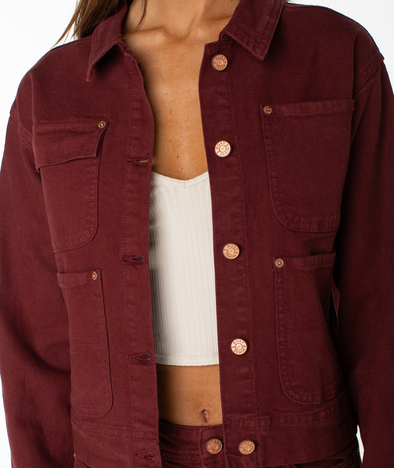 A person wearing the Roxy Reel Life Jacket, a maroon cropped jacket with oversized pockets, layered over a white ribbed crop top, shown from shoulders to hips against a white background.