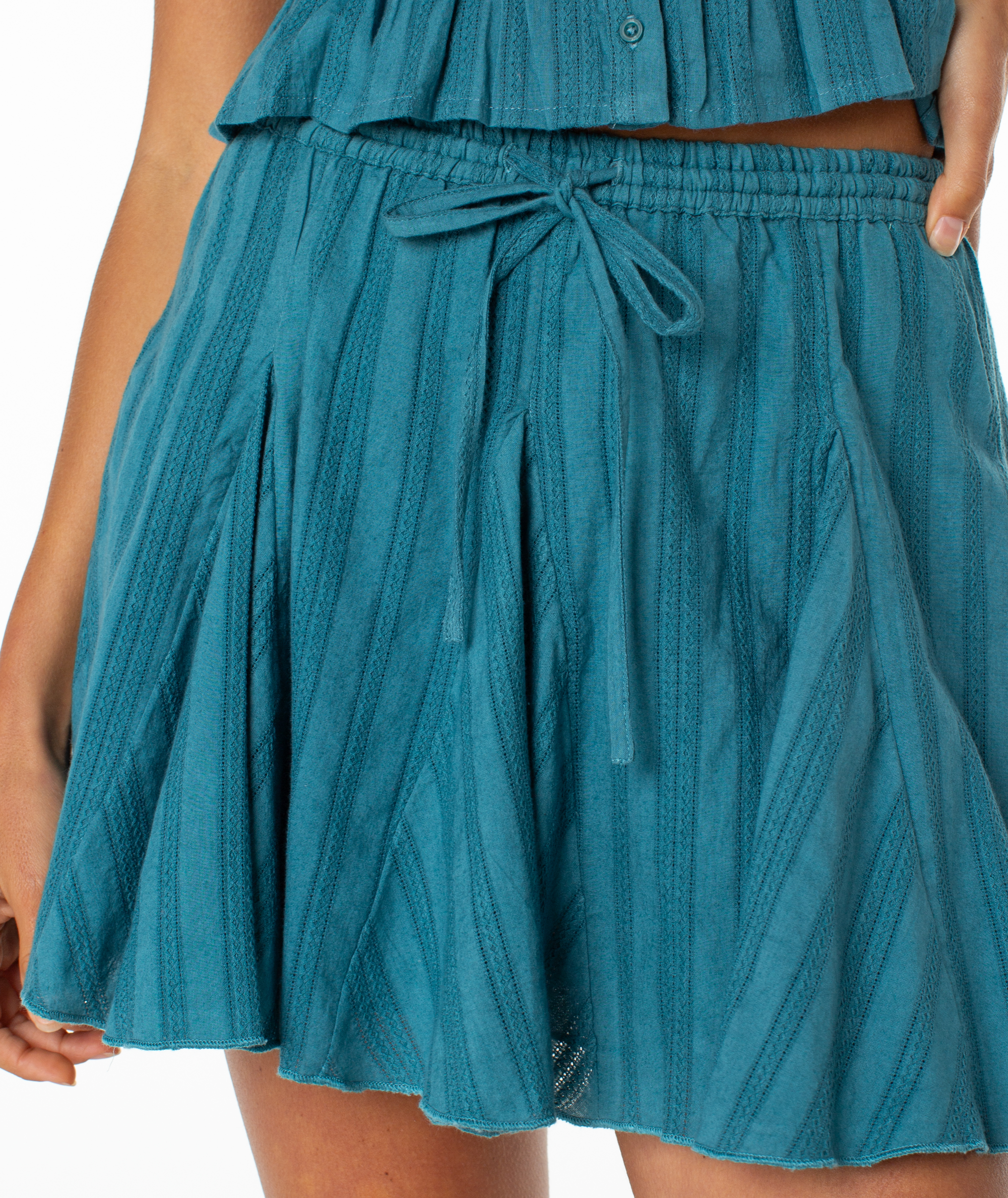 Someone wears the Roxy Forever Dreamin Skirt—a teal, pleated, textured coastal skirt with a tie front at the waist—paired with a matching top, shown from waist to mid-thigh.