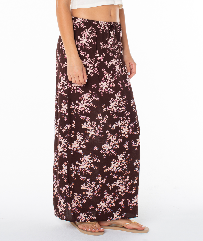 A person wears a white crop top and the Iyla Skirt by Roxy in Tulipwood Evening Meadow, paired with sandals, standing against a white background.
