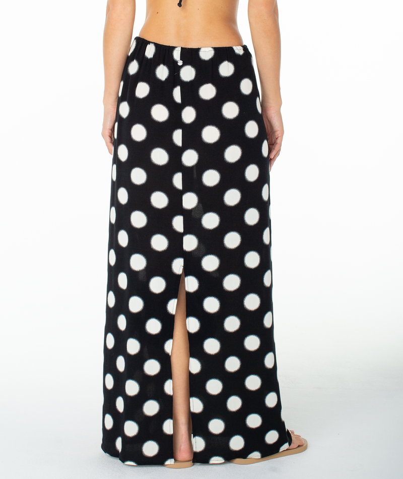 A person wearing the Roxy Iyla Skirt—featuring bold white polka dots on black fabric and a back slit—is seen from behind. The chic tie waist of this skirt by Roxy flatters the silhouette, adding style to its playful design.