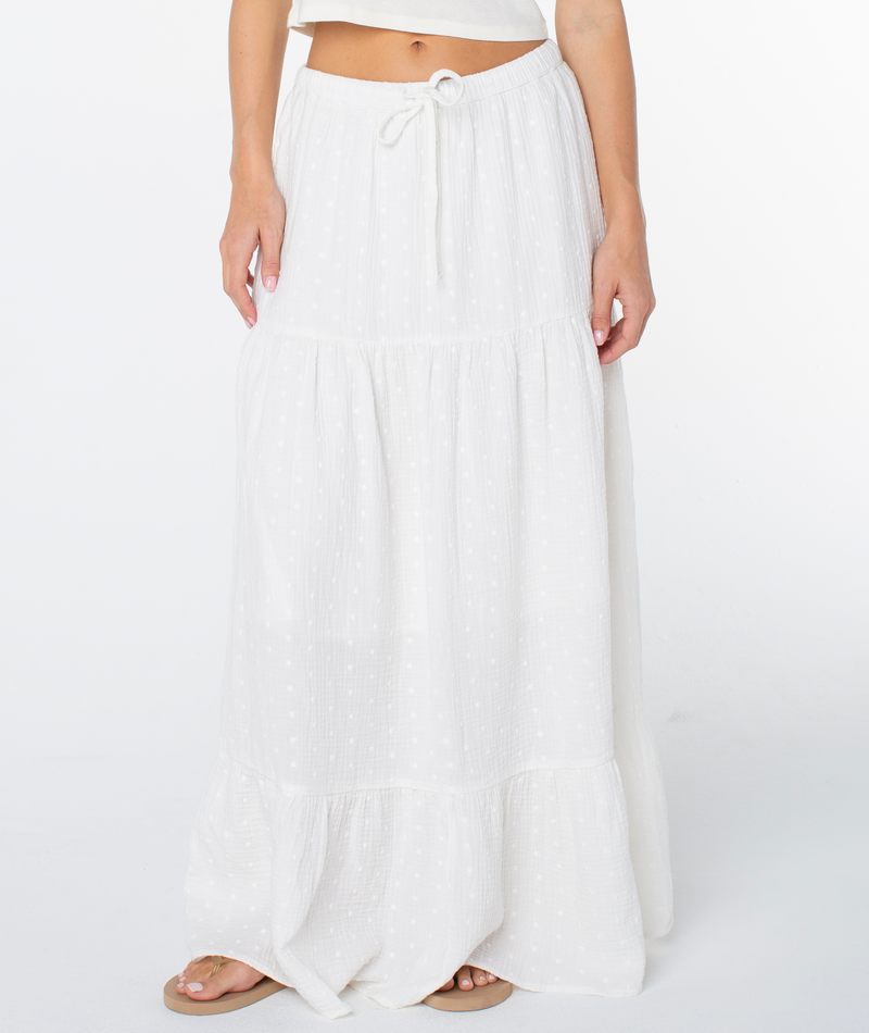 A person wearing the Roxy Side Street Skirt, a long white tiered maxi with a drawstring waist and textured design, paired with a white top and tan sandals, stands against a white background.