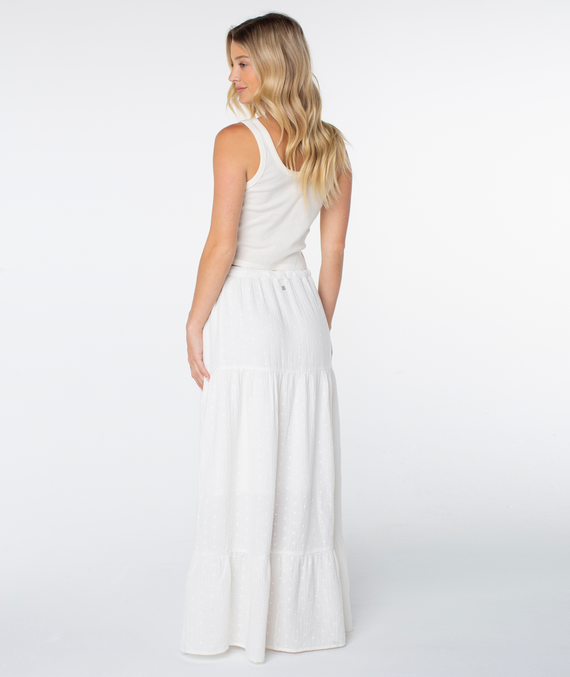 A woman with long blonde hair models the Roxy Side Street Skirt, wearing it with a white sleeveless top as she stands turned away on a plain white background.