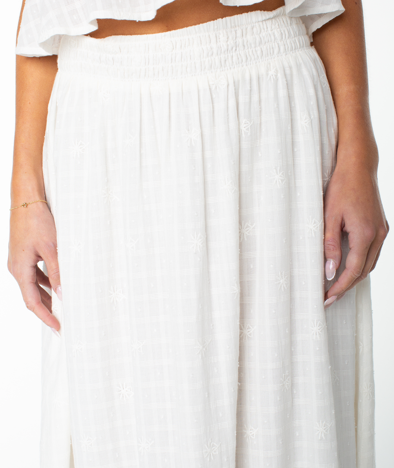 A person wearing the Roxy Sophie Maxi Skirt—a white, high-waisted, flowy maxi skirt with subtle embroidered patterns—stands with arms relaxed at their sides against a white background.