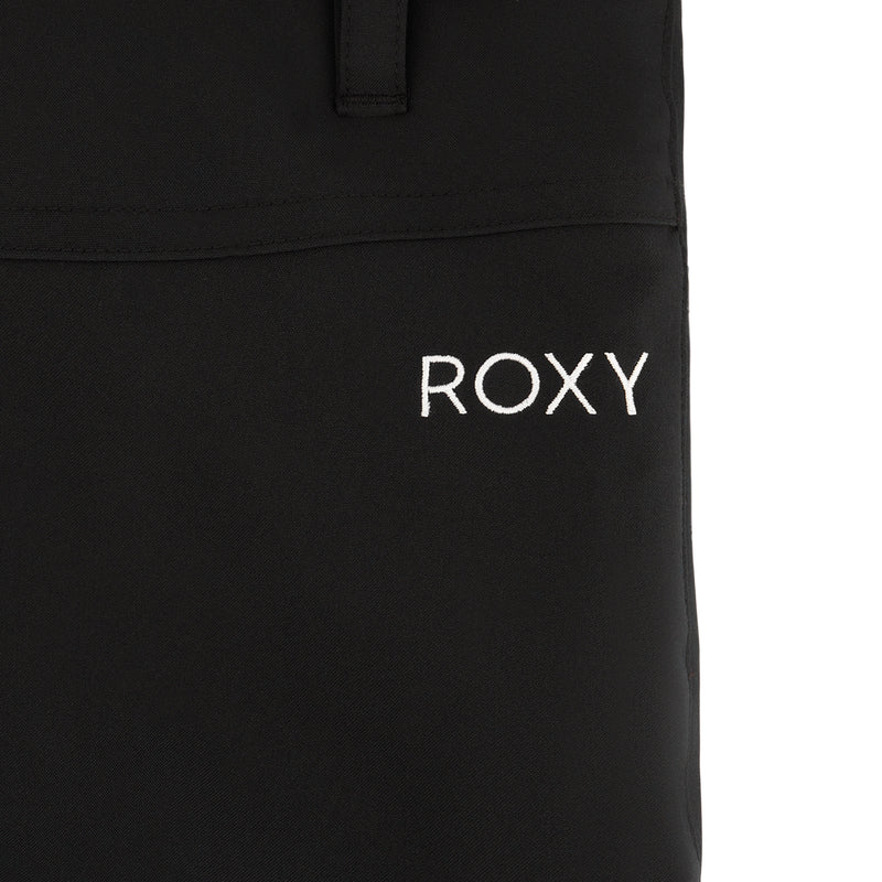 Close-up of black fabric from the Roxy Girls' Backyard Pant with "ROXY" embroidered in white uppercase letters. A seam and part of an adjustable waistband loop or strap are visible at the top of the image.