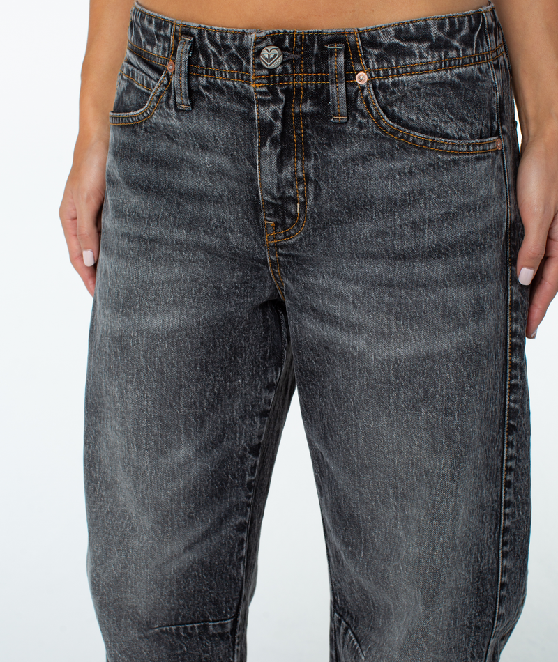A person models Roxy Surf Pipe Pant—high-waisted, faded black with copper stitching and a subtle barrel leg—against a white background, cropped to show only the lower torso and upper legs.