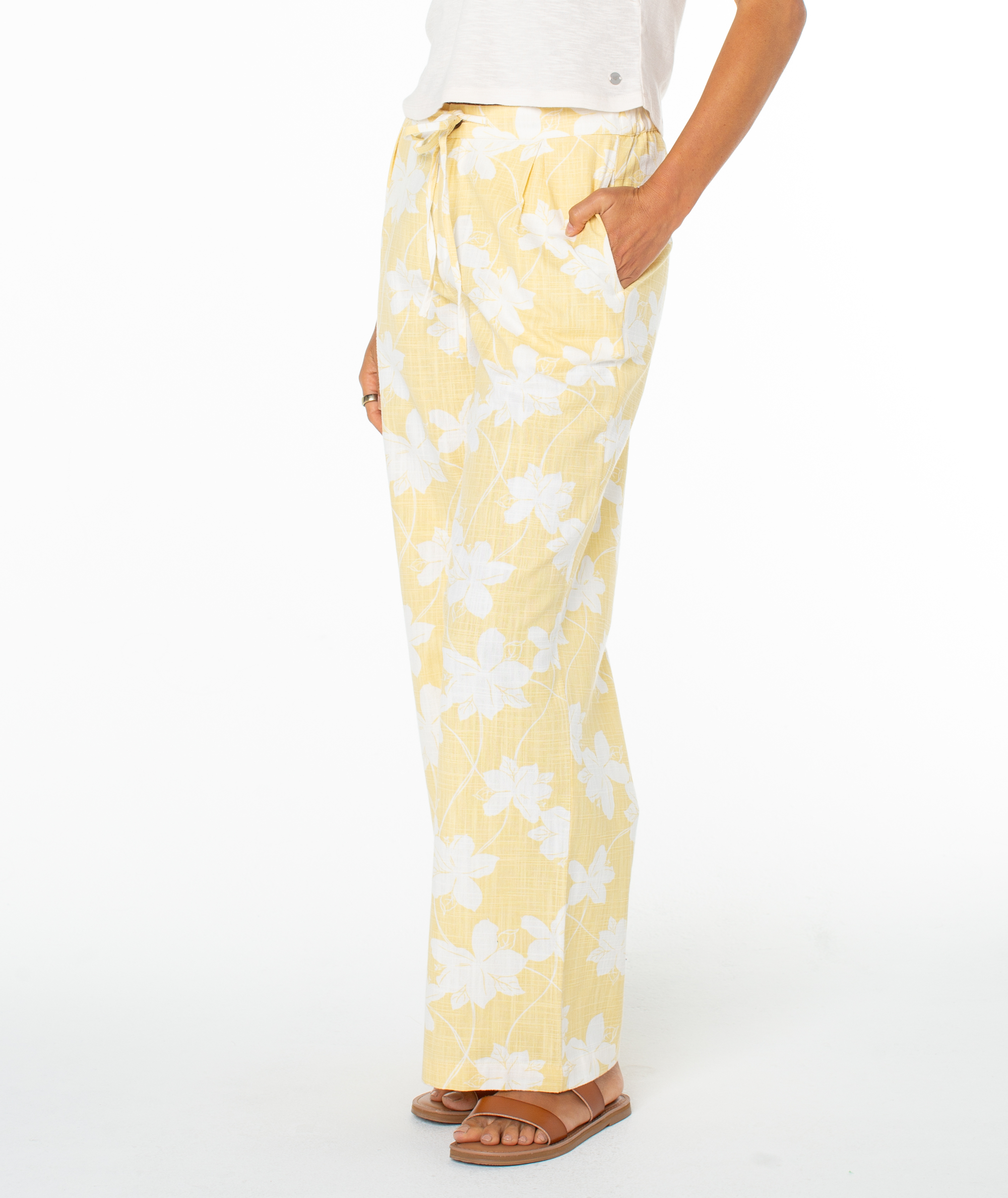 A person wears Roxy's Mavericks Trouser, featuring a light yellow floral print, wide-leg fit, and drawstring waist, paired with a white top and brown sandals. These statement summer pants are perfect for warm days.