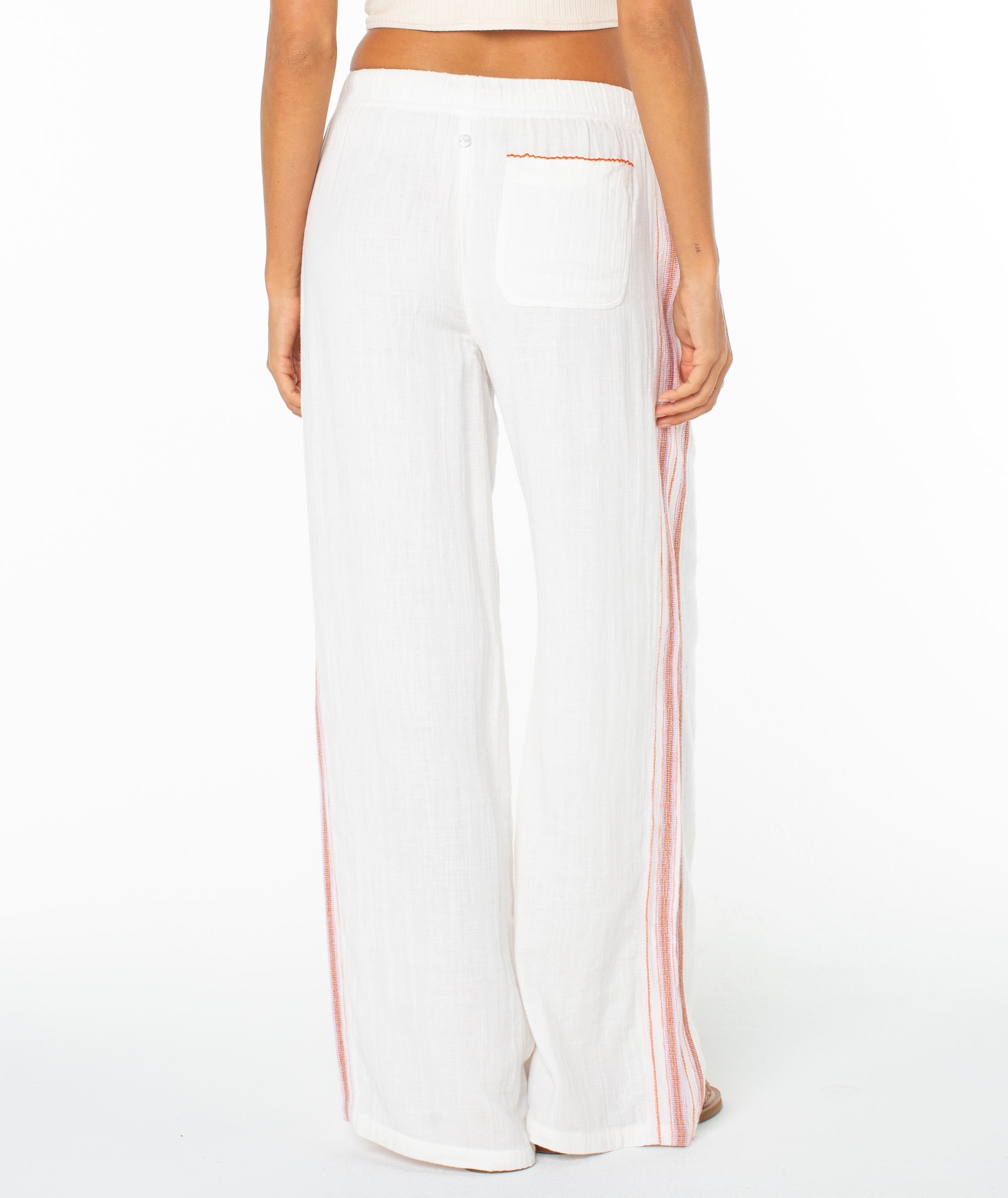 A person wearing Roxy Fiesta Siesta Pant—white, wide-leg summer pants with red side stripes and a back pocket trimmed in red—shown from the back against a plain white background.