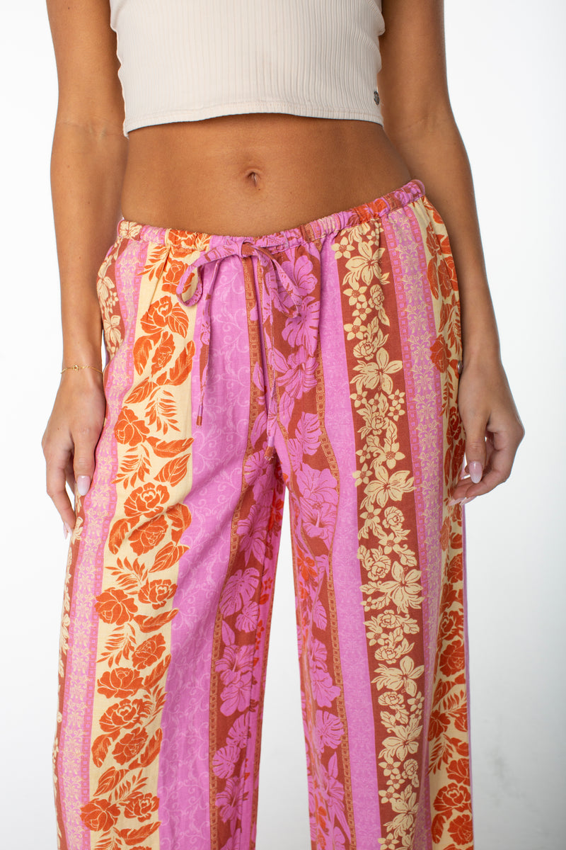 A person is wearing the Roxy Iyla Pant 2 with vertical pink, red, orange, and beige floral stripes, paired with a light beige ribbed crop top. Only the torso and upper legs are shown.