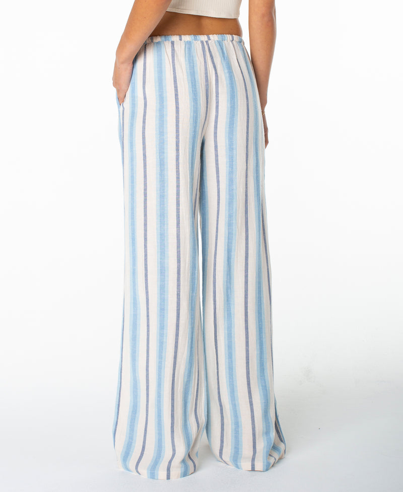 A person is shown from the back wearing the Roxy Iyla Pant 2—a pair of loose, wide-leg pants with vertical blue and white stripes. These relaxed-fit pants feature an elastic waistband and capture a breezy coastal style, as the individual stands against a plain white background.