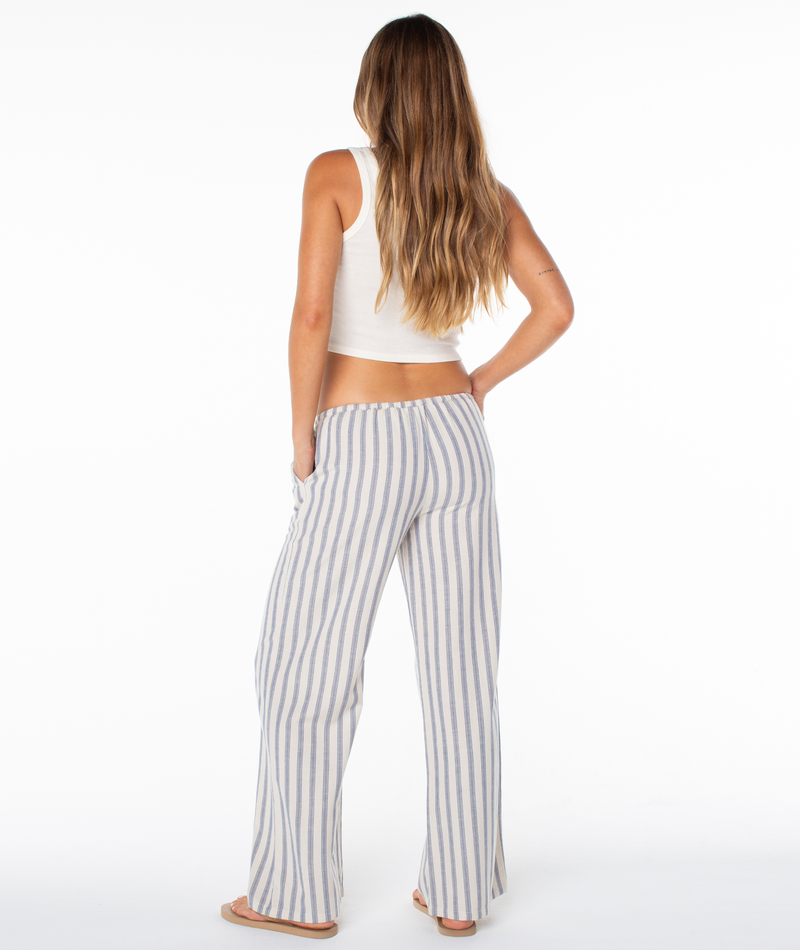 A woman from behind wears a white tank top and blue and white striped Roxy Iyla Pant 2 with side slits at the hems.
