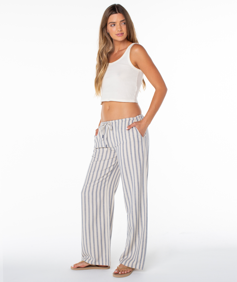 A person wears a white cropped tank top and Roxy Iyla Pant 2, which are relaxed fit, blue and white striped drawstring pants.