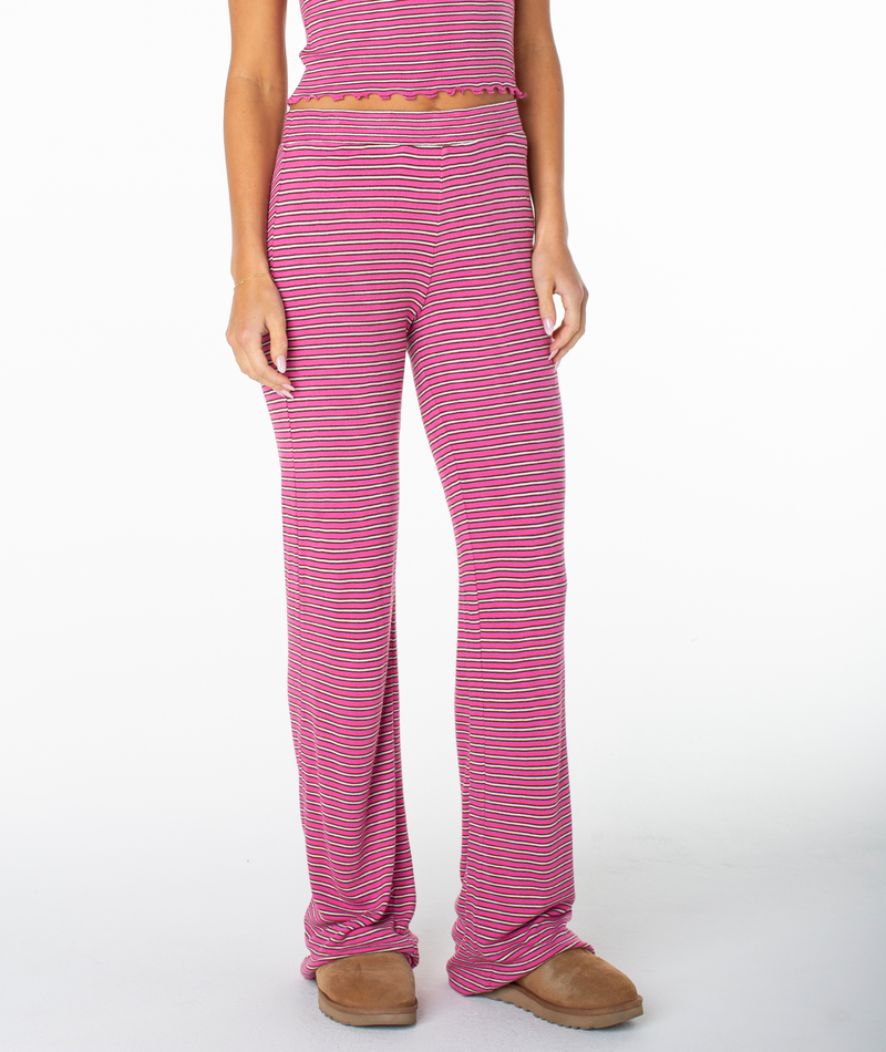 A person is seen wearing the Roxy Summer Fling Rib Pant 2 in Ibis Rose Rewind Stripe, paired with brown slippers, standing against a plain white background. The image focuses on the lower torso and legs, adding a hint of coastal flair to the scene.
