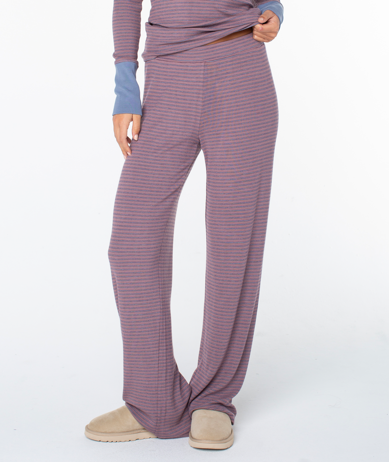 A person wears the Roxy Summer Fling Rib Pant 2—loose, high-waist purple and grey striped loungewear—paired with a matching long-sleeve top and tan slippers; only the lower half is visible against a white background.