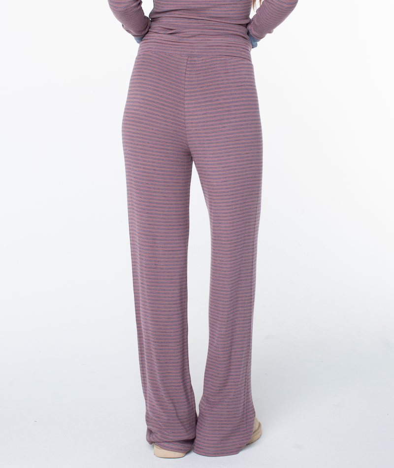A person stands on a white background, seen from the back, wearing the Roxy Summer Fling Rib Pant 2 in mauve and gray stripes with a high waist.