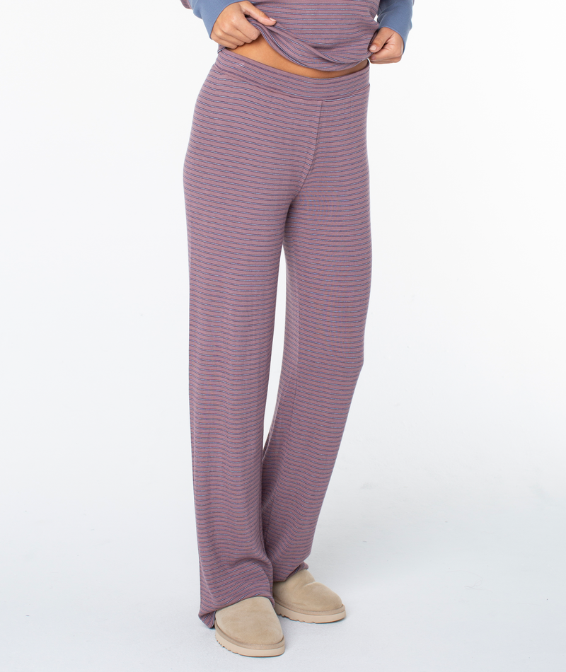 A person models the Roxy Summer Fling Rib Pant 2—loose, high-waisted, purple and gray striped loungewear with wide legs—paired with beige slippers against a plain white background. Only the lower body is shown.