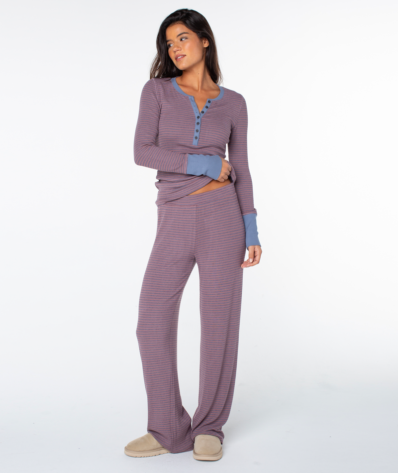 A woman wears the Roxy Summer Fling Rib Pant 2 in Twilight Mauve Pinstripe with beige slippers, standing against a plain white background.