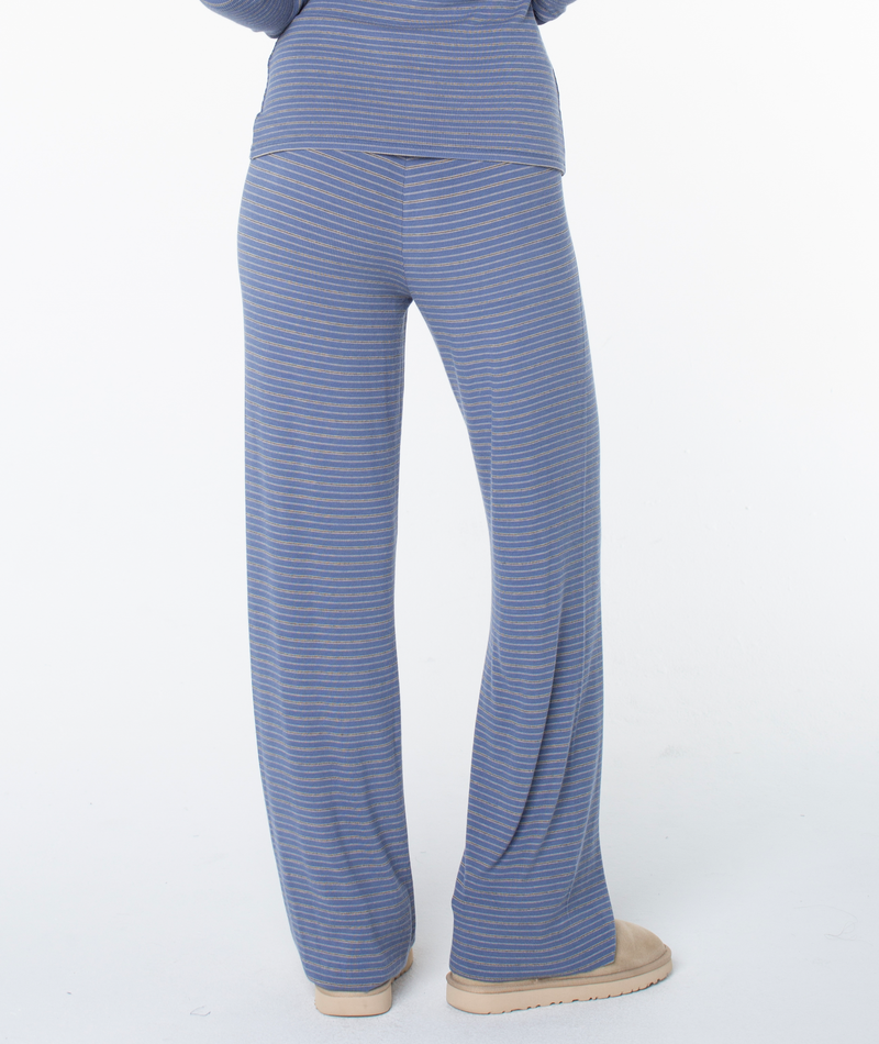 A person stands with their back to the camera, wearing Roxy’s Summer Fling Rib Pant 2 in blue and gray stripes paired with beige shoes, set against a white background.