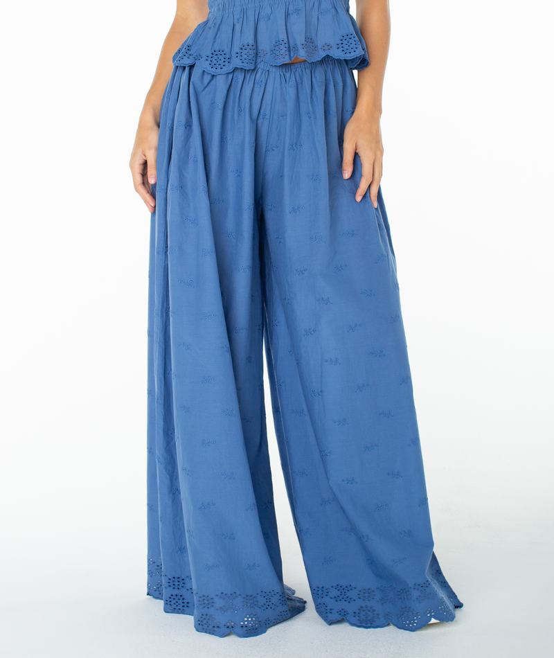 Person wearing the Roxy Cambria Pant in Dutch Blue Solid, featuring loose, flowy tailoring with a scalloped eyelet hem and subtle embroidered pattern; relaxed fit with a glimpse of the matching top.