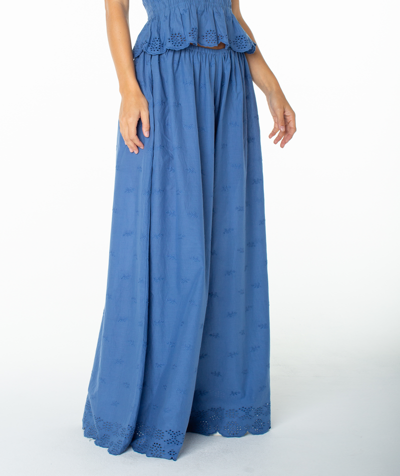 A person wearing the Roxy Cambria Pant—a blue, high-waisted, wide-leg style featuring eyelet detailing at the hem and waist that evokes relaxed tailoring—stands against a plain white background.