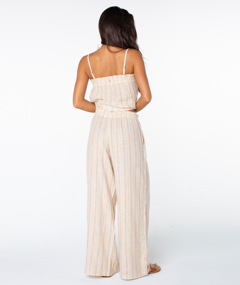 A woman with long dark hair faces away, wearing a beige sleeveless striped top and Roxy Offshore Pant with sandals, set against a plain white background.