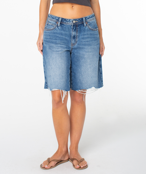 A person wearing Roxy's Lifesaver Short in Salt Fade Denim Wash, a grey cropped top, and brown flip-flops stands against a plain white background.