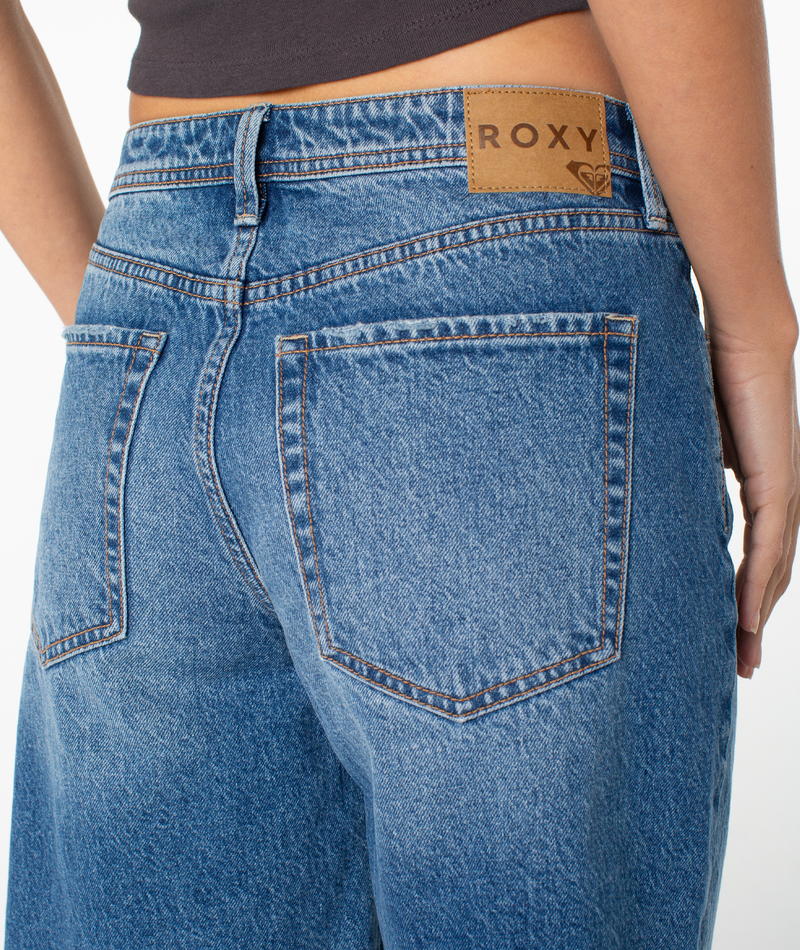 Close-up of a person wearing Roxy Lifesaver Short midrise denim shorts with a brown leather brand patch on the waistband, paired with a black crop top.