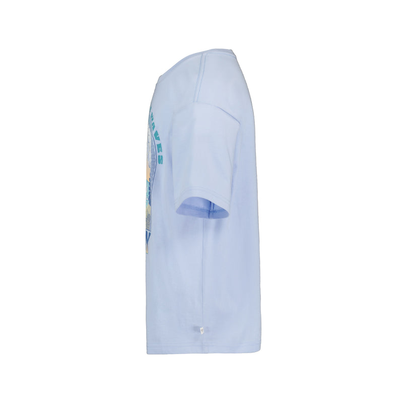 The Girls' Chasing Waves Oversized Tee by Roxy is shown from the side facing right, in light blue cotton jersey with partial graphic and text on the front and sleeve, set against a plain white background.